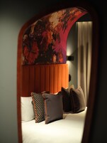 Una cama con cabecera naranja y almohadas estampadas, un tapiz floral y vistas de una cortina.