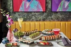 Variedad de platos de sushi sobre una mesa, un florero rosa con flores y una copa de cóctel.