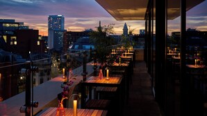 An outdoor terrace with wooden tables and chairs, candles, and a cityscape view in the background. - Malmaison Manchester Deansgate  (Manchester)