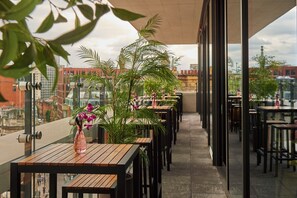 A terrace with wooden tables and chairs, a potted plant, and a view of the cityscape. - Malmaison Manchester Deansgate  (Manchester)