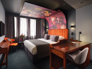A modern hotel room with a large bed, a desk, and a chair. There is a large window with curtains, a wall-mounted TV, and a decorative wall piece. - Malmaison Manchester Deansgate  (Manchester)