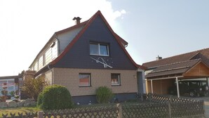 Una casa de dos pisos con techo inclinado, una chimenea a la vista y un pequeño porche delantero.