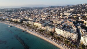 An aerial view of a coastal city with a beachfront hotel, dense urban area, and clear blue waters. - Apartment with Partial Sea View – Sunset – Cannes Croisette – Palais Miramar (Cannes)