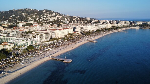 Un paisaje urbano costero con una playa extensa, un muelle y una colina con edificios.