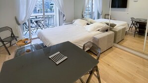 A modern bedroom with a large bed, a desk, and a balcony with outdoor furniture. - Apartment with Partial Sea View – Sunset – Cannes Croisette – Palais Miramar (Cannes)