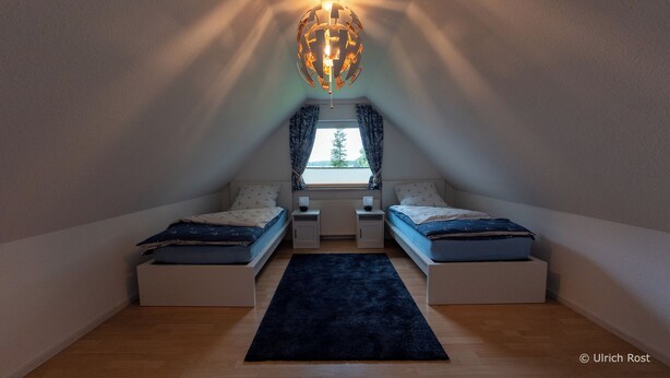 Una camera da letto mansardata accogliente e piccola, con due letti, una finestra con tende e un'originale lampada a forma di globo, con vista sull'esterno.
