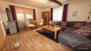 Un accogliente soggiorno con un tavolino in legno, un divano con cuscini decorati, un'area pranzo con sedie e un mobiletto.
