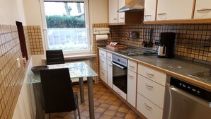 A compact kitchen with a dining table, chairs, a stove, oven, and a dishwasher. - Vacation apartment Ramke EG (Lilienthal)