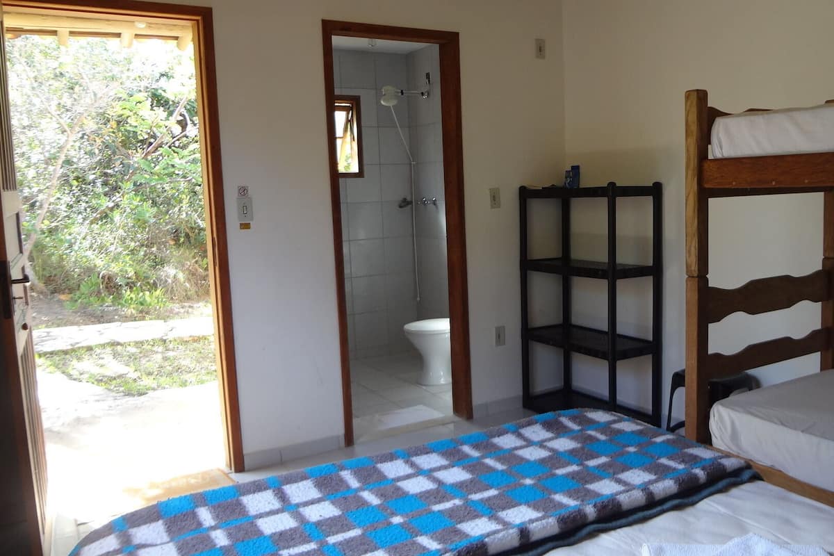 A room with a bunk bed, a small bathroom with a shower, and a shelf unit.