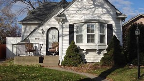 A white two-story house with a front porch, a small front yard, and a mailbox. - 2 Blks St Marys 2 Main Fl Beds Bath CoveredByFaith (Rochester)