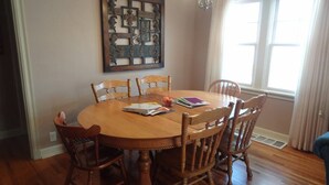 A dining room with a round wooden table and six chairs, a decorative wall piece above the table, and a window with curtains. - 2 Blks St Marys 2 Main Fl Beds Bath CoveredByFaith (Rochester)