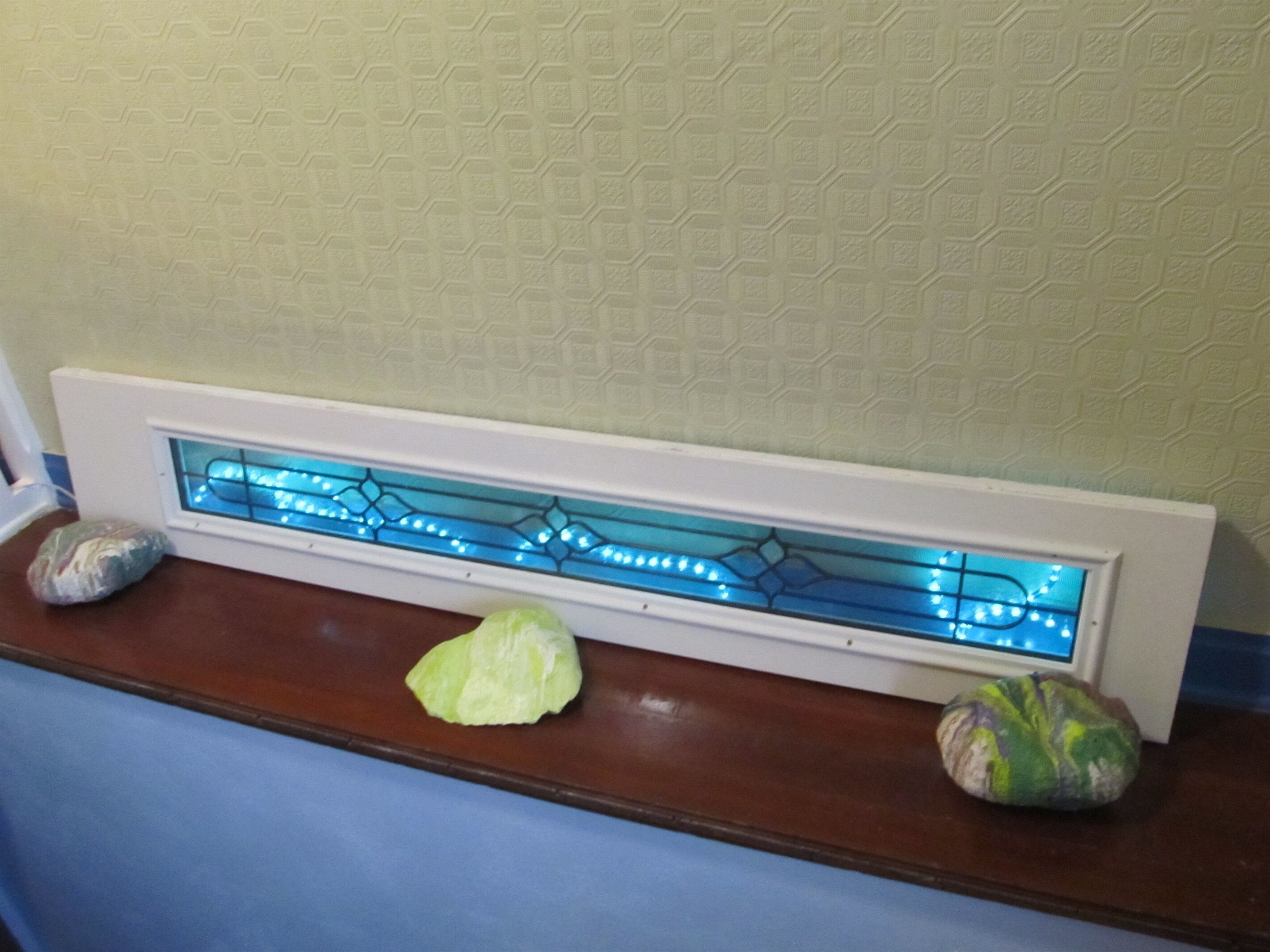 Un baño con tocador blanco, encimera azul y un panel de vidrio decorativo con luces azules.