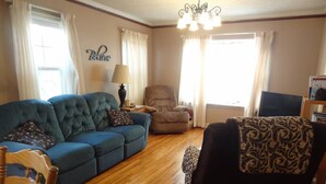 A living room with a blue sofa, a patterned armchair, a wooden coffee table, and a lamp. - 2 Blks St Marys 2 Main Fl Beds Bath CoveredByFaith (Rochester)