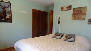 Un dormitorio con una cama, dos almohadas con estampados de ciervos, una puerta de madera y una pared con tres cuadros.