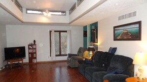 A living room with a wooden floor, a sofa, a TV, a bookshelf, and a painting on the wall.