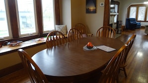 Una sala da pranzo con tavolo e sedie in legno, una finestra con tende, una libreria e una sedia blu sullo sfondo.