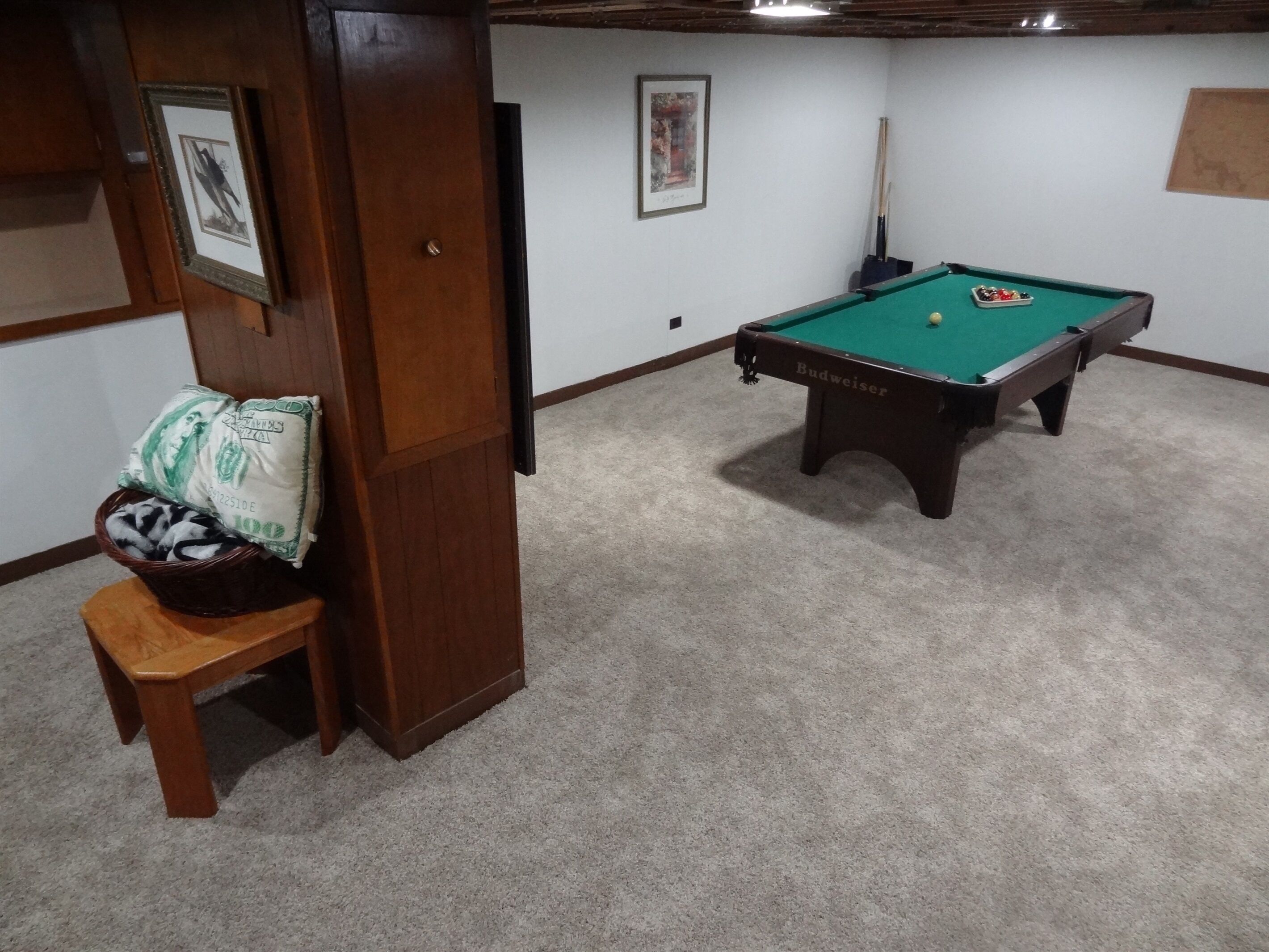 Une pièce avec une table de billard, une chaise en bois et un mur orné d’un tableau encadré.