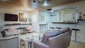 Een moderne woonkamer met een bank, fauteuils, een salontafel, een televisie en een plafondventilator.