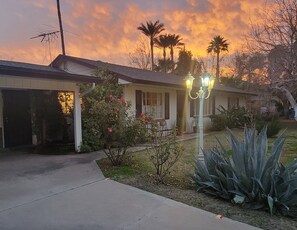A single-story house with a garage, a front porch, and a well-maintained garden with various plants and a small tree. - RazInn Central Phoenix (Phoenix)
