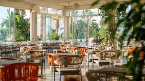 A spacious restaurant with multiple tables and chairs, large windows offering views of lush greenery and palm trees. - Agaya Bodrum +16 Adult Only (Ex.Prive Bodrum) - All inclusive (Bodrum)