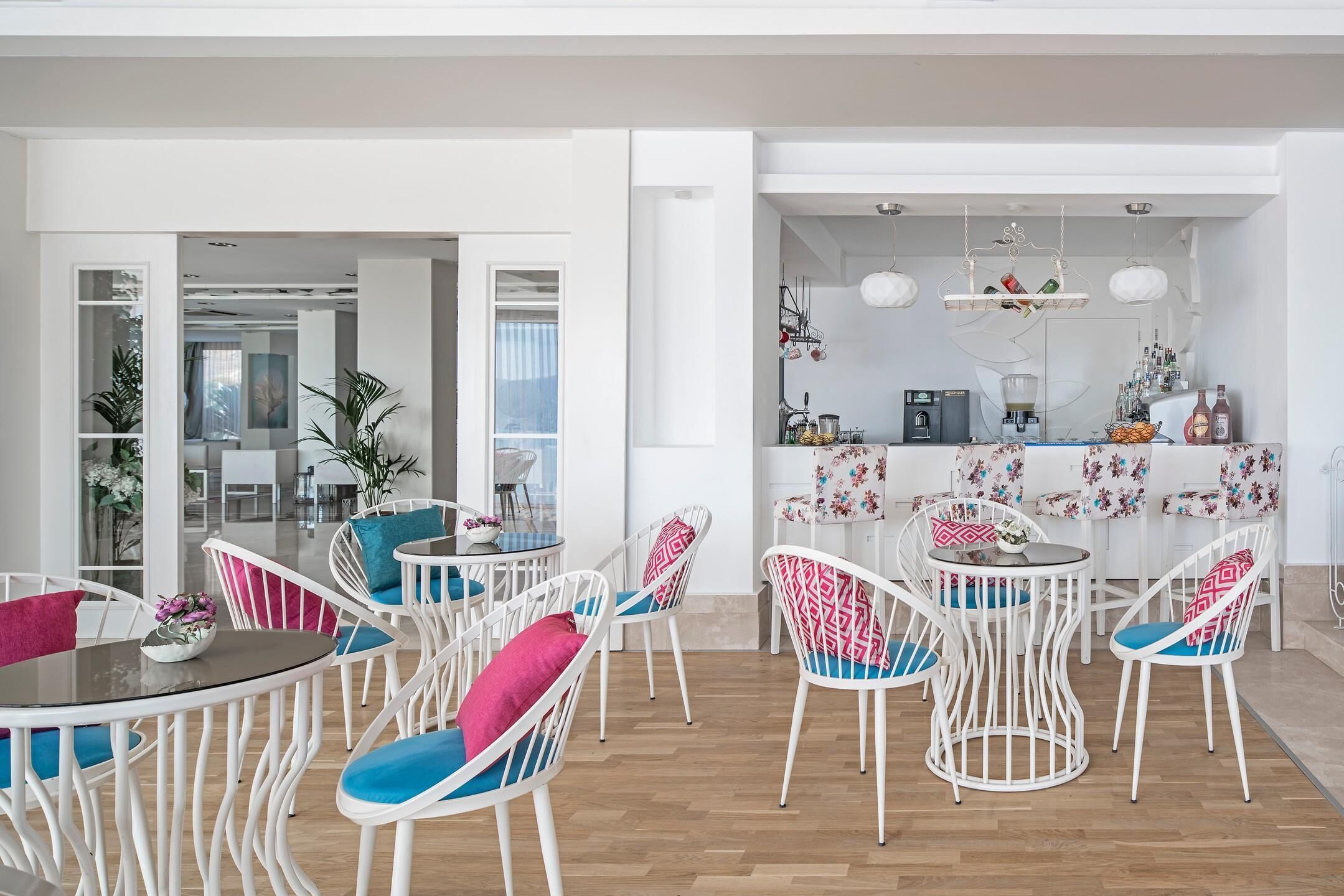 Un espace repas moderne avec des chaises blanches et des coussins bleus, une table ronde et un coin cuisine équipé d’un bar et de divers appareils électroménagers.
