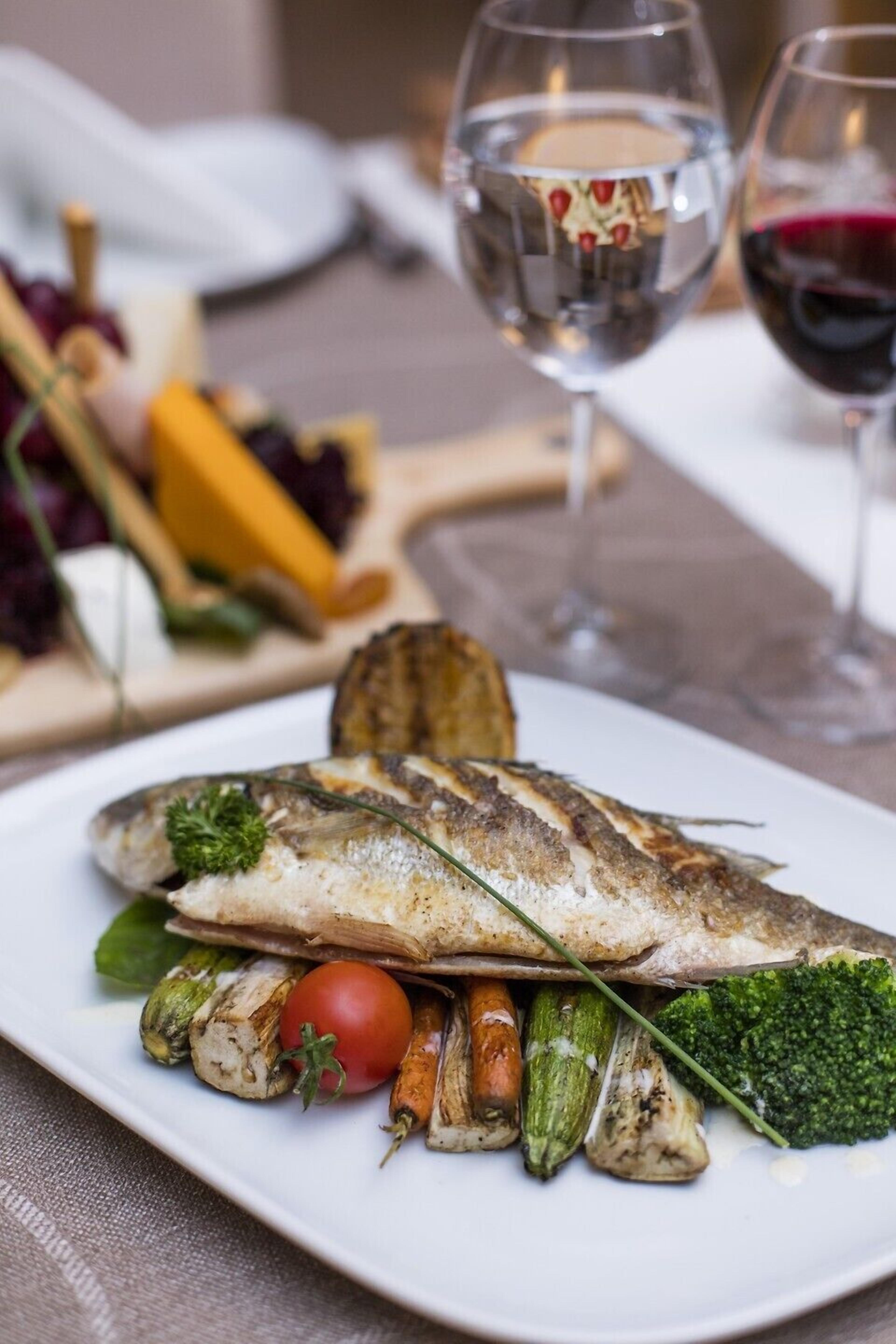 Un piatto di pesce alla griglia con verdure e un bicchiere di vino rosso.