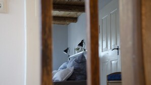 Un couloir étroit avec un plafond en bois, une porte blanche et un lit avec un matelas bleu.