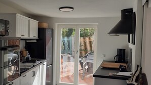 Une cuisine moderne avec des armoires blanches, une hotte noire et une porte-fenêtre coulissante donnant sur une terrasse extérieure.