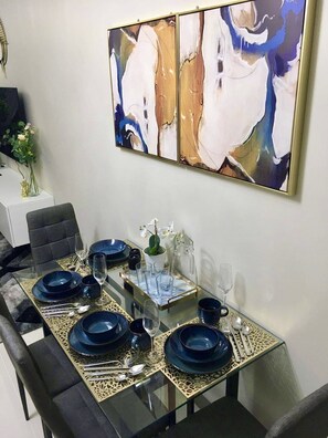 A dining area with a glass table set for six, featuring blue plates and clear glasses. - New & Modern Cozy 1BR w/ Balcony in Uptown BGC (Taguig)
