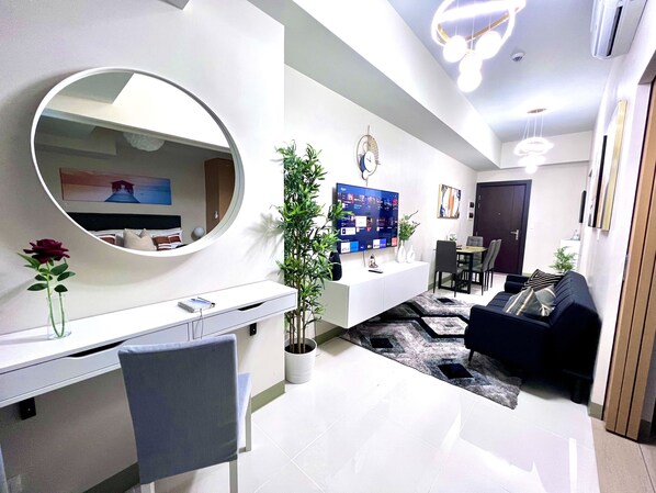 A modern living room with a round mirror, a potted plant, a TV, and a sofa. - New & Modern Cozy 1BR w/ Balcony in Uptown BGC (Taguig)
