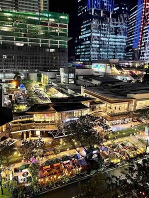 A modern urban hotel with multiple floors, outdoor dining areas, and a river view. - New & Modern Cozy 1BR w/ Balcony in Uptown BGC (Taguig)