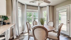 A dining area with a round table, four chairs, a ceiling fan, and large windows with curtains. - Elegant home in the heart of Westfield! Perfect for family gatherings! (Westfield)