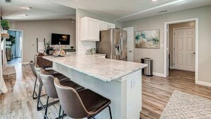 A modern kitchen with a central island, bar stools, stainless steel appliances, and a large painting on the wall. - Elegant home in the heart of Westfield! Perfect for family gatherings! (Westfield)