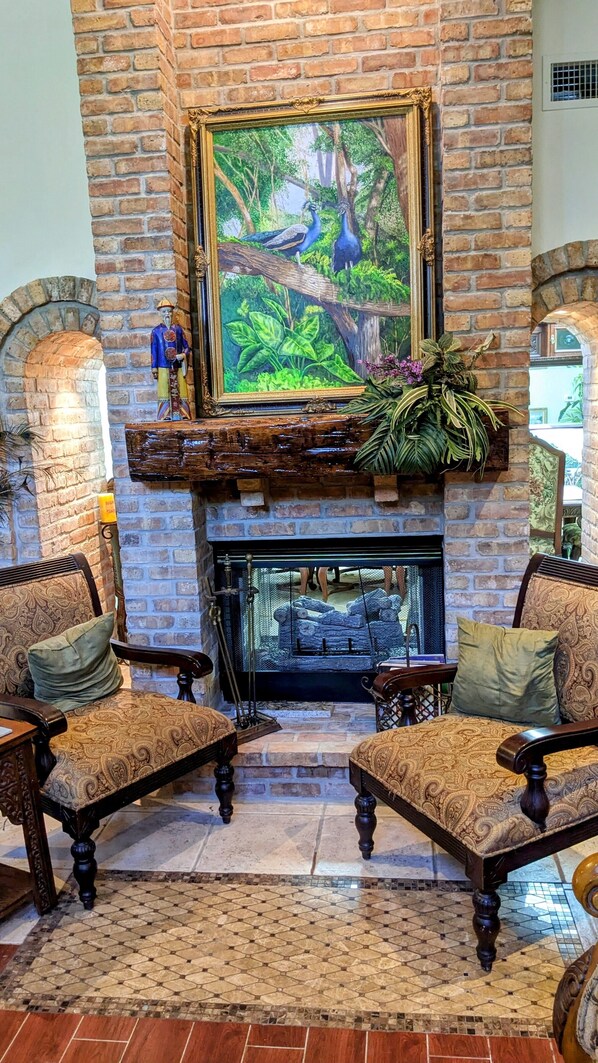 A fireplace with a painting above it, two upholstered chairs, and a decorative plant on the mantel.