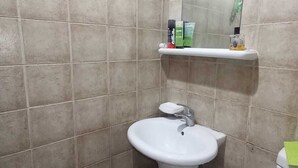 Casa de banho com uma pia branca, um espelho e uma prateleira com artigos de higiene pessoal.