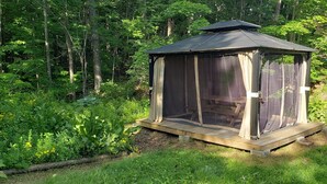 Un belvédère en bois doté d’une véranda grillagée, situé dans un cadre forestier luxuriant et verdoyant.