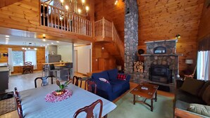 Un intérieur de chalet chaleureux comprenant un coin repas, un salon, une cheminée en pierre et une cuisine.