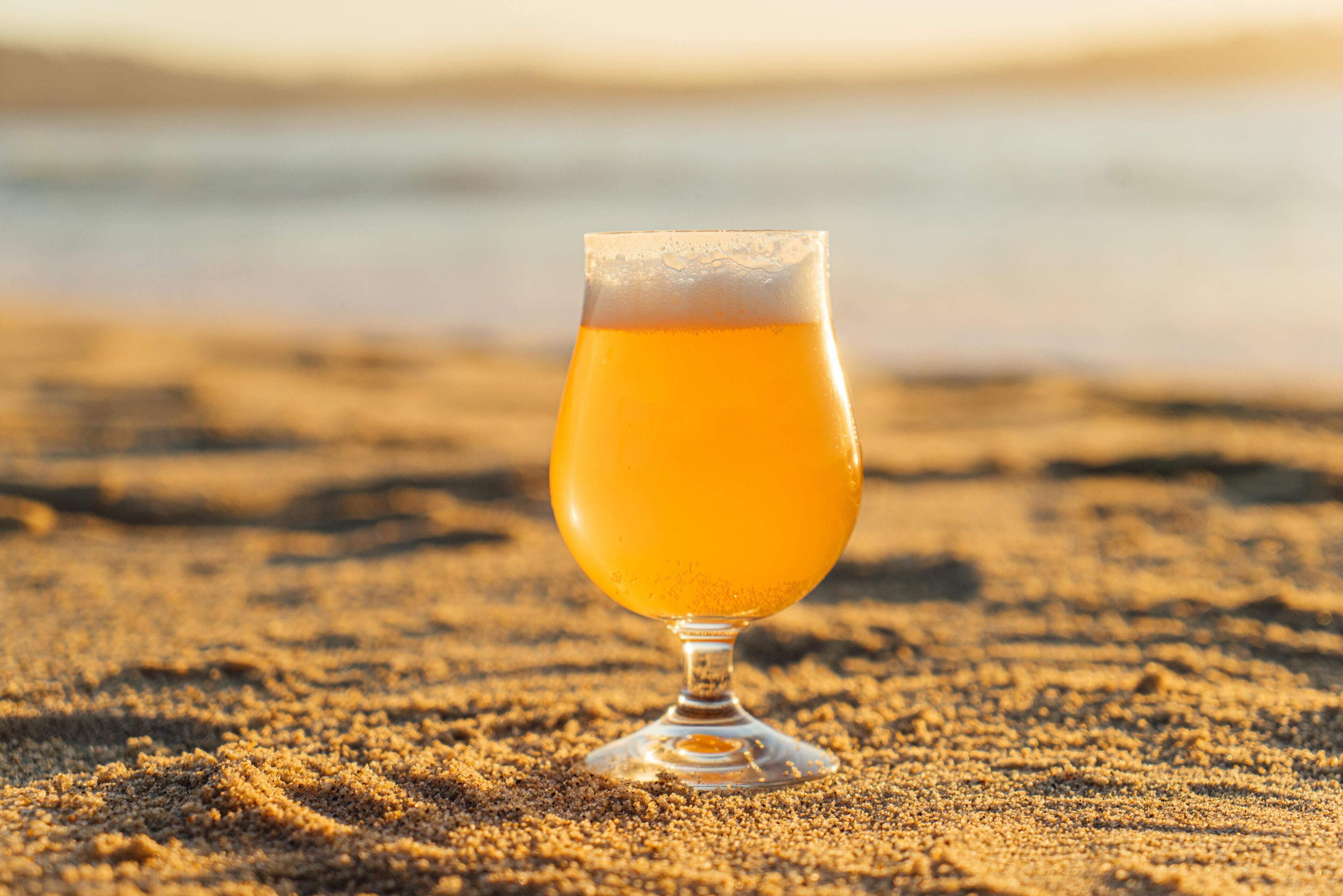 A glass of amber liquid on a sandy surface.