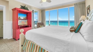 Habitación de hotel con una cama grande, televisión, ventilador de techo y balcón con vista al océano.