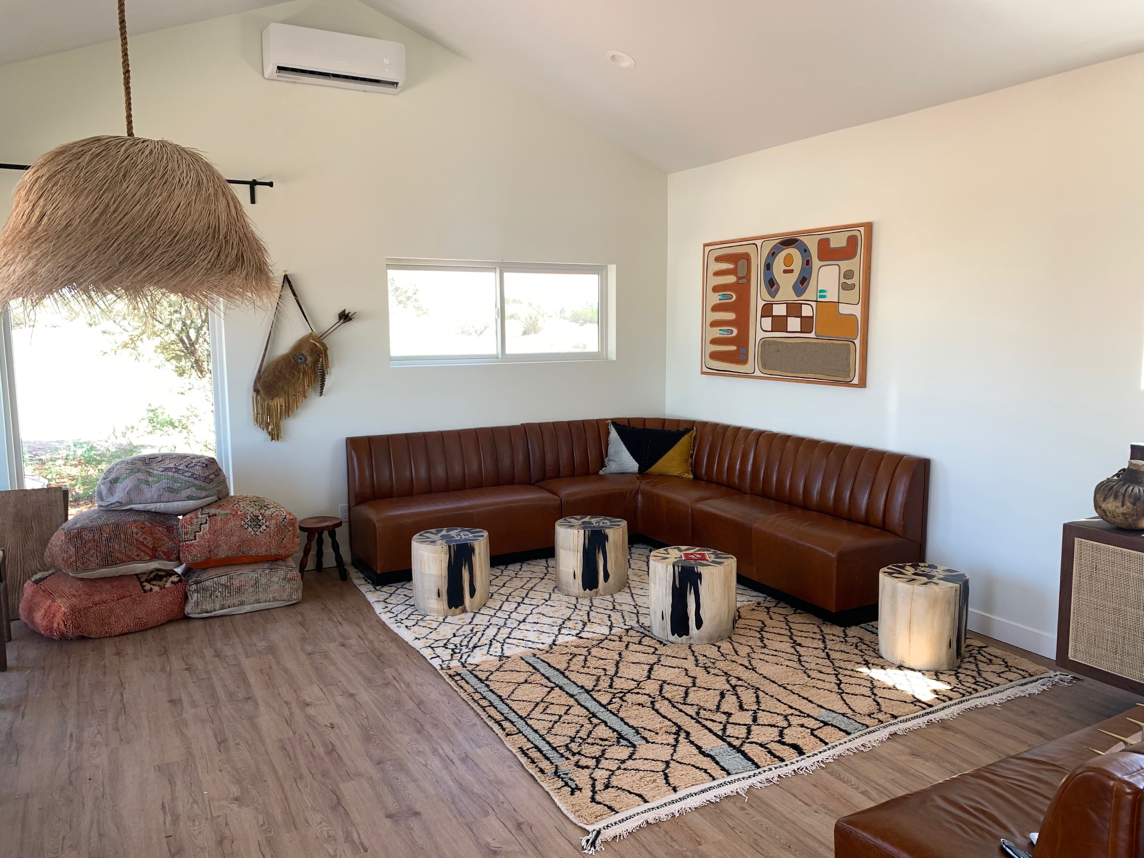 A modern living room with a brown leather sectional sofa, a patterned rug, and a hanging light fixture.