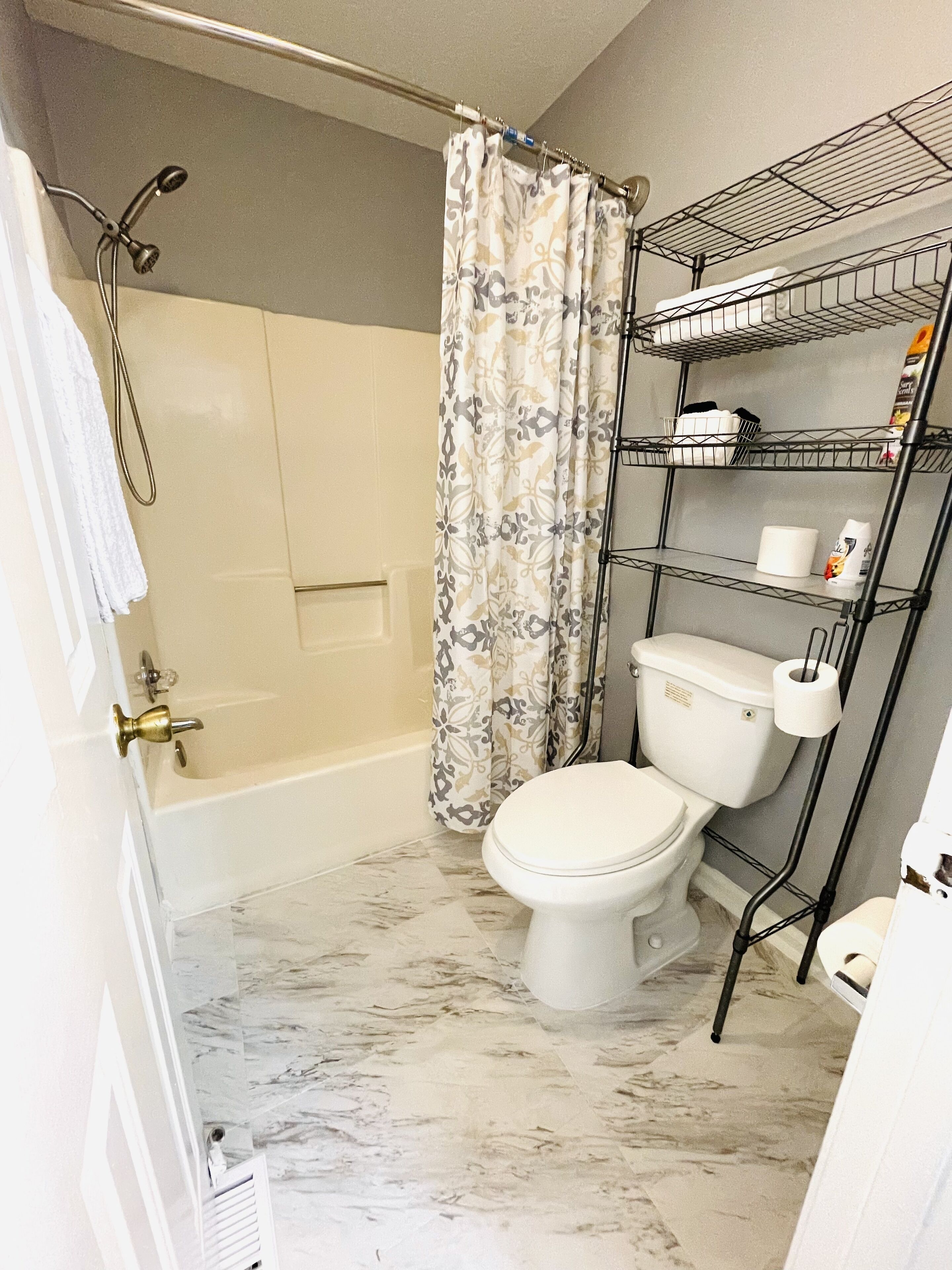 A bathroom with a shower, toilet, and a shelf unit.
