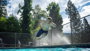 Une personne qui saute dans une piscine entourée d’une clôture en treillis métallique et d’arbres.