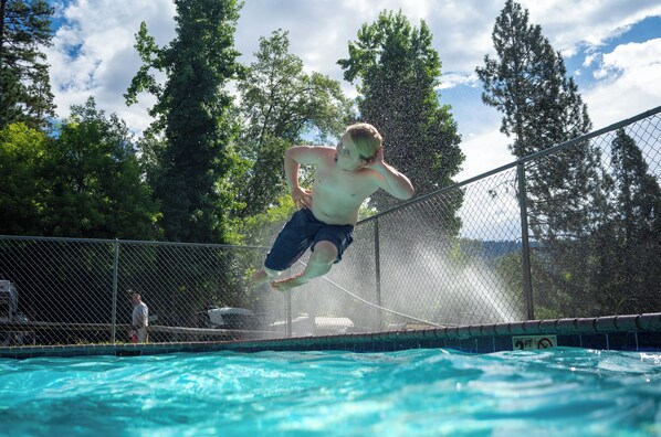 A person jumping into a swimming pool surrounded by a chain-link fence and trees. - Outdoorsy Yosemite (Bass Lake)