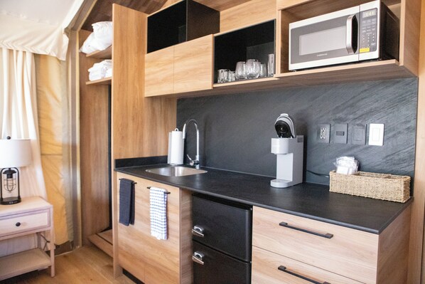 A modern kitchen with a black countertop, wooden cabinets, a microwave, and a coffee maker.