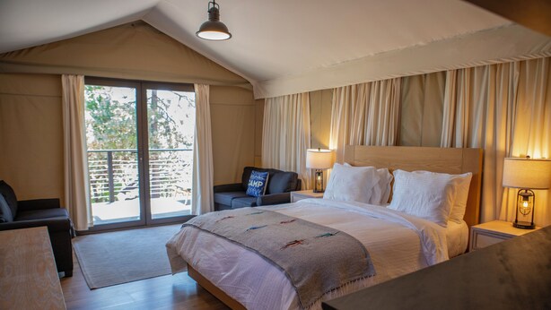 Une chambre avec un grand lit, une table de chevet avec une lampe, une chaise et une vue sur l’extérieur grâce à une porte coulissante.