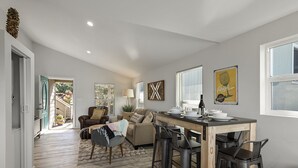 A spacious living area with a dining table, bar stools, and a sofa. There is a staircase leading to an outdoor area. - Forest Heights ~ Relaxed Modern-Boho Style, Forest Views, Hot Tub, Wine Country (Forestville)