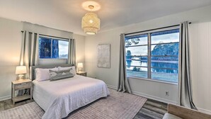 Ein Schlafzimmer mit einem großen Bett, zwei Nachttischen mit Lampen, einem Fenster mit Vorhängen und Blick auf einen See.