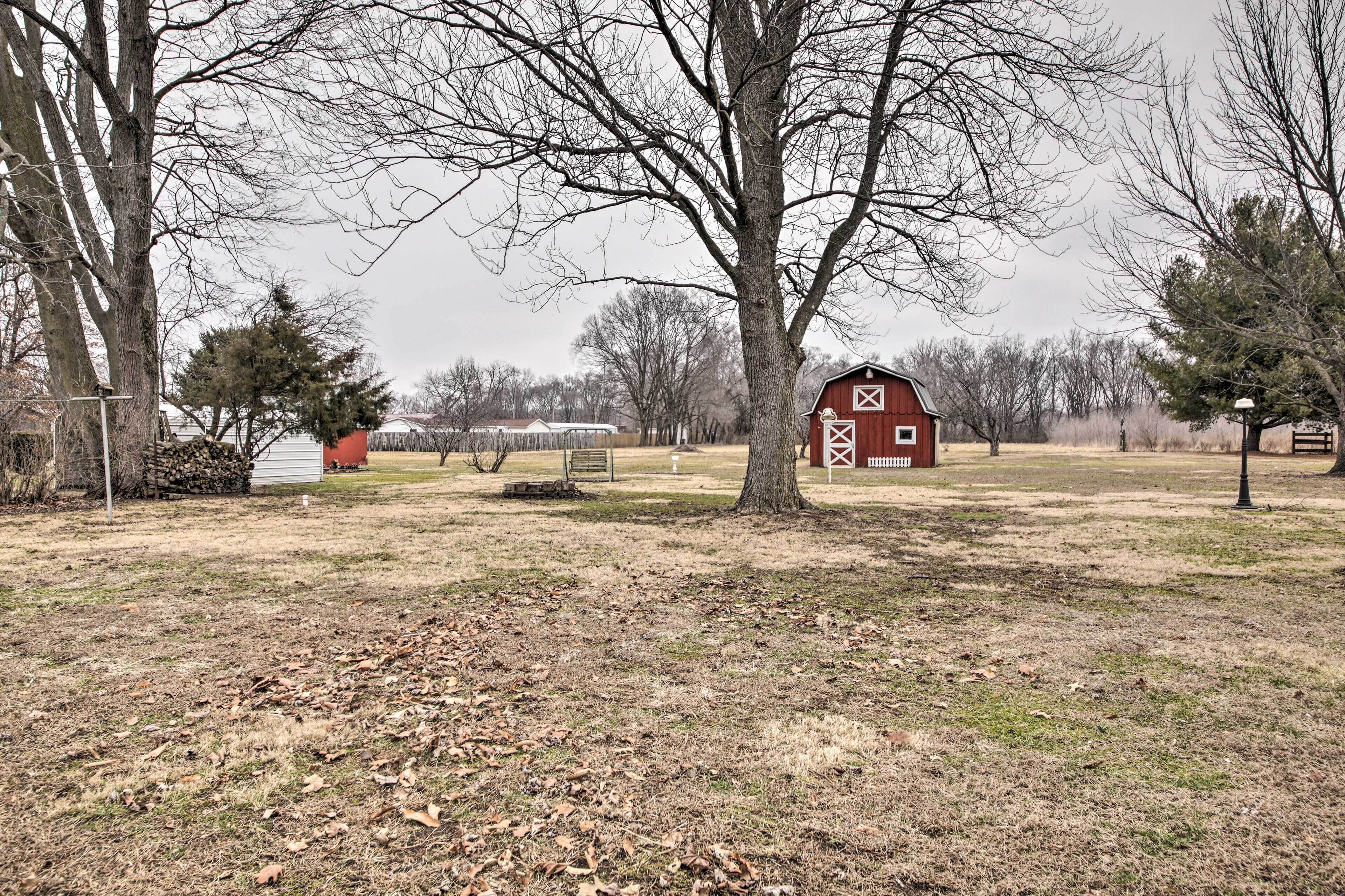 Un paysage rural avec une grange rouge, un grand arbre et un petit bâtiment blanc en arrière-plan.
