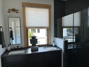 A modern bathroom with two sinks, a large mirror, and a shower area.
