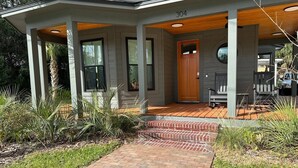 Uma casa moderna com varanda coberta, um caminho de tijolos até a entrada e uma porta de madeira.
